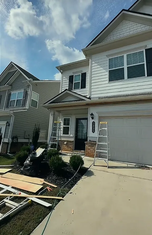 Townhouse exterior during trim repair, with ladders set at the porch and replacement fascia and trim boards laid out on the driveway