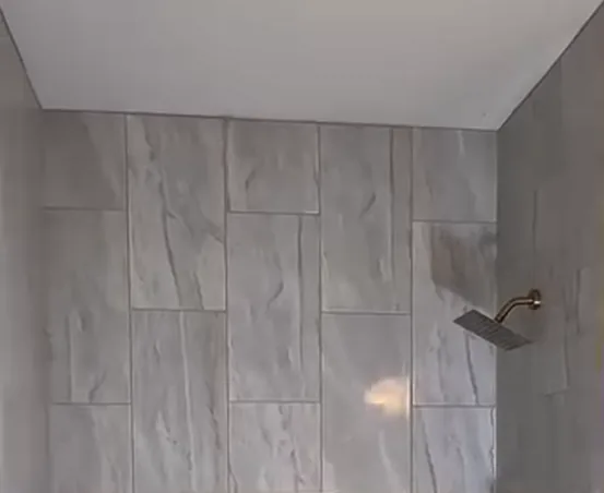 Gray marble-look large-format tile shower wall with a square brushed gold rain shower head on a matching gold arm